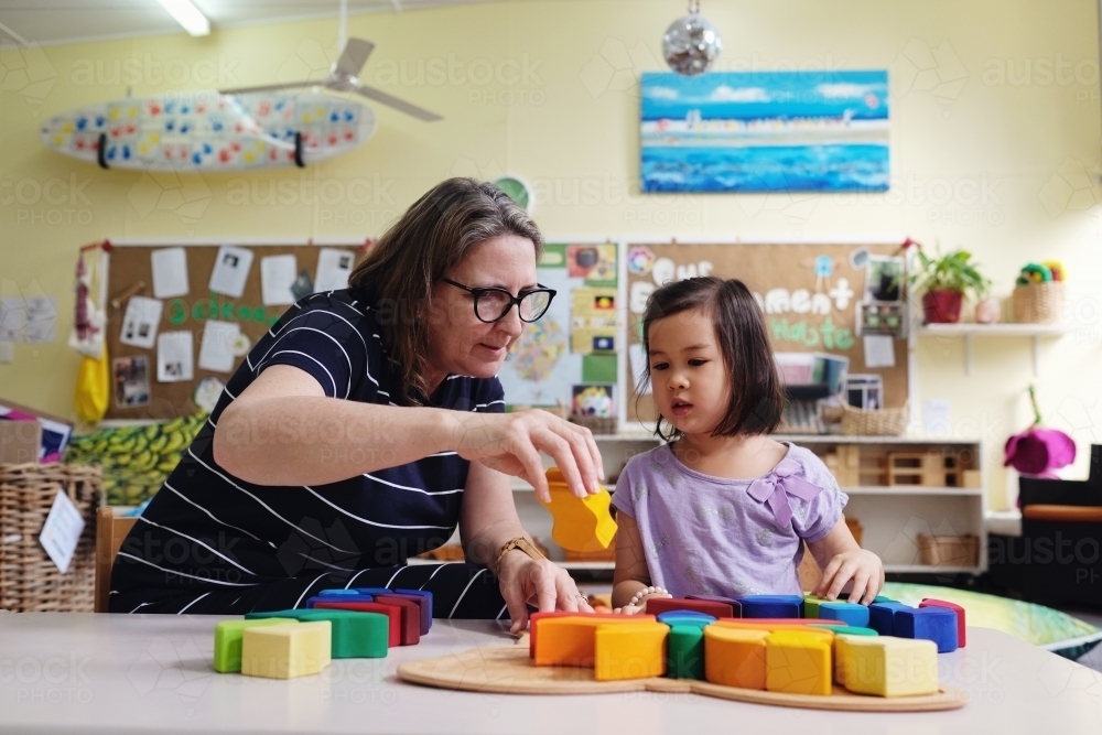 Multicultural teacher and child playing wooden blocks puzzles in kindergarten - Australian Stock Image