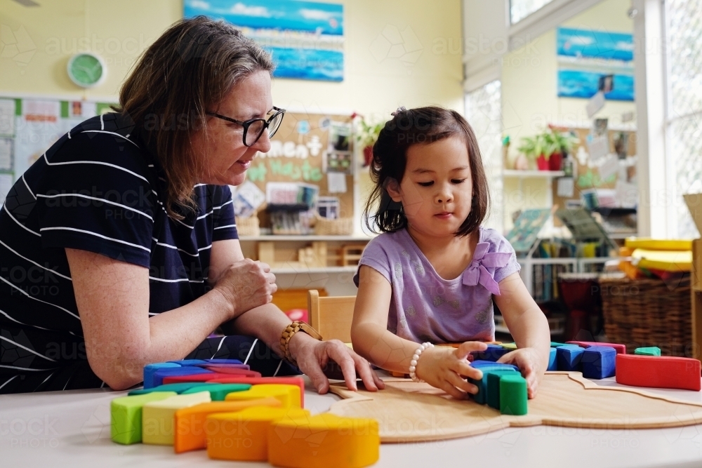 Multicultural teacher and child playing wooden blocks puzzles in kindergarten - Australian Stock Image