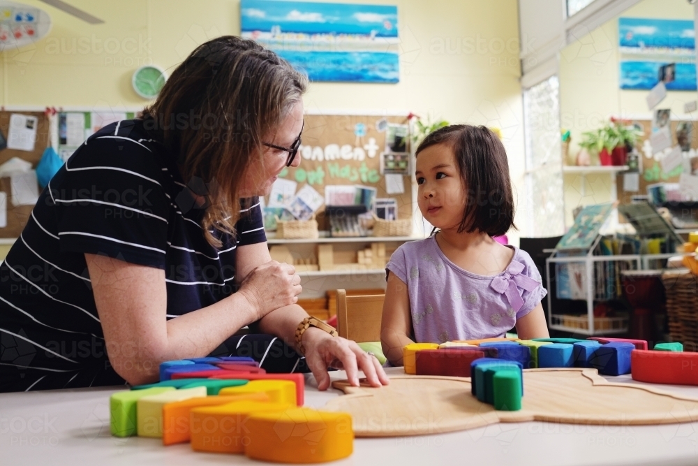 Multicultural teacher and child playing wooden blocks puzzles in kindergarten - Australian Stock Image