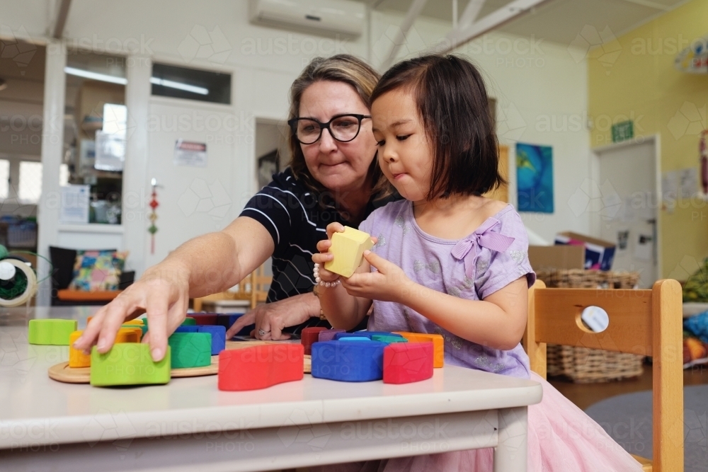 Multicultural teacher and child playing wooden blocks puzzles in kindergarten - Australian Stock Image