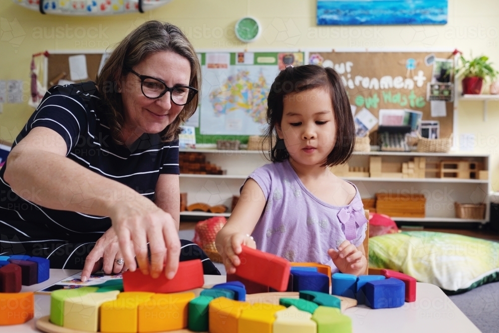 Multicultural teacher and child playing wooden blocks puzzles in kindergarten - Australian Stock Image