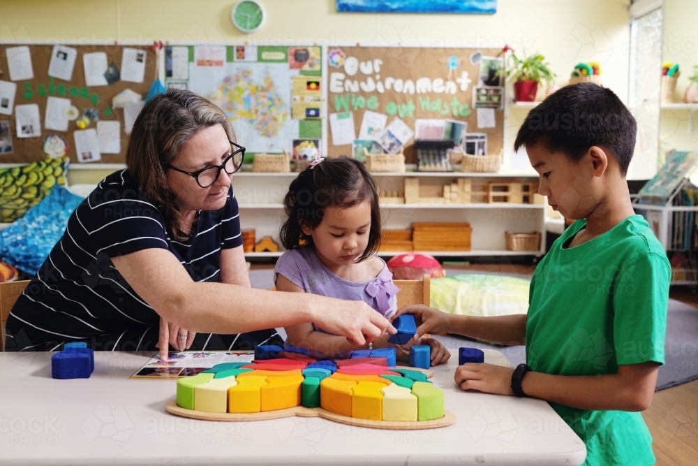 Multicultural teacher and children playing wooden blocks puzzles in kindergarten - Australian Stock Image