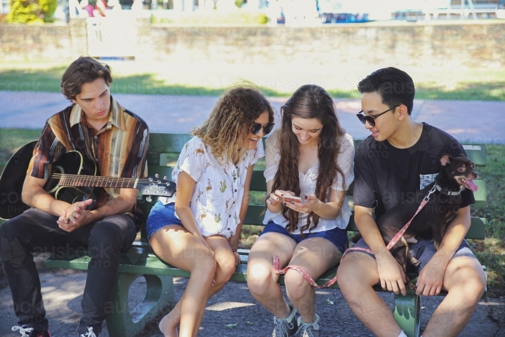 Multicultural teenagers hanging out and using mobile phone - Australian Stock Image