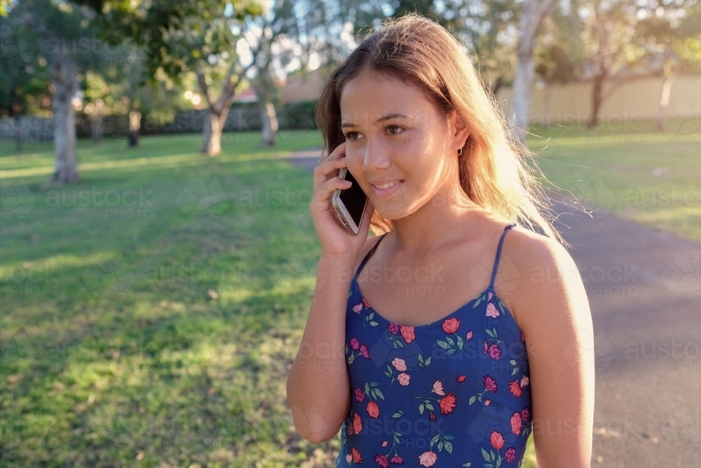 Multiethnic teenage girl using phone in the park - Australian Stock Image