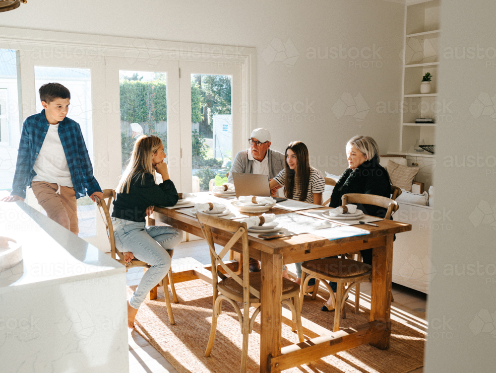 Multigeneration family gathered in the dining table while working on the computer. - Australian Stock Image