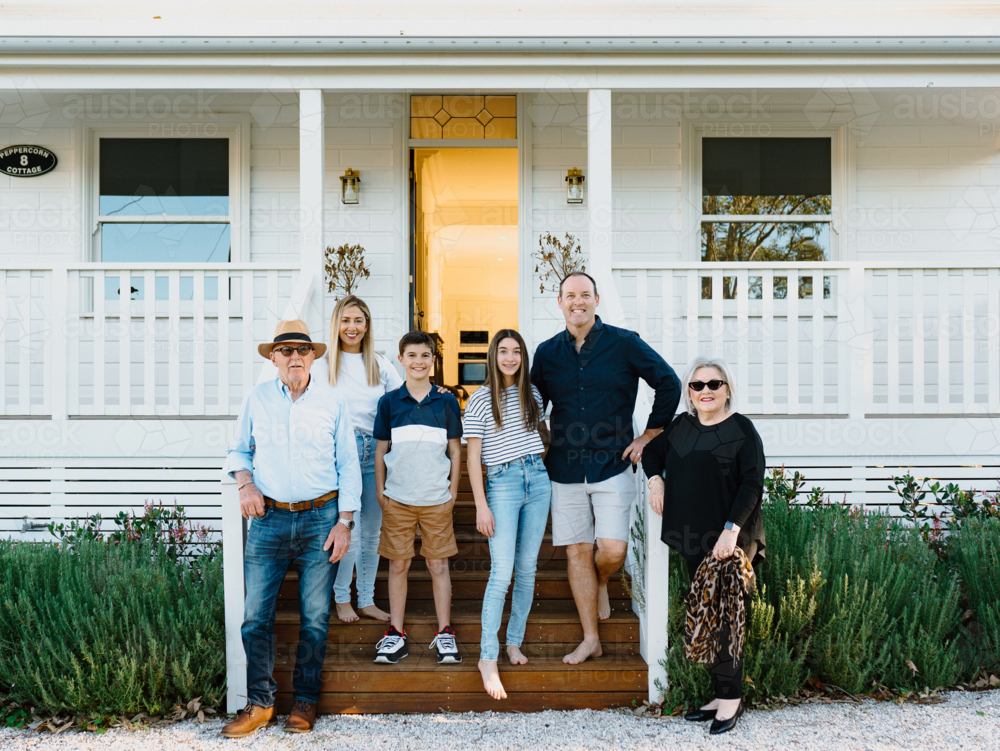 Multigeneration family standing on a wooden step of their porch. - Australian Stock Image