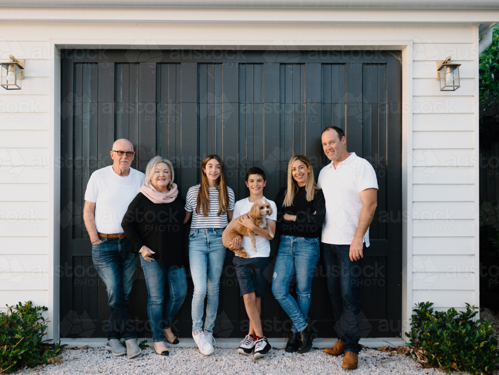 Multigenerational family standing outside in front of black garage door - Australian Stock Image