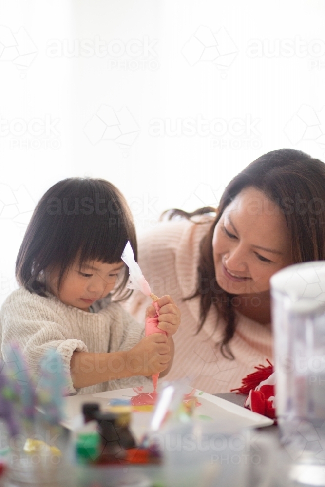 Mum and daughter decorating cookies at home - Australian Stock Image