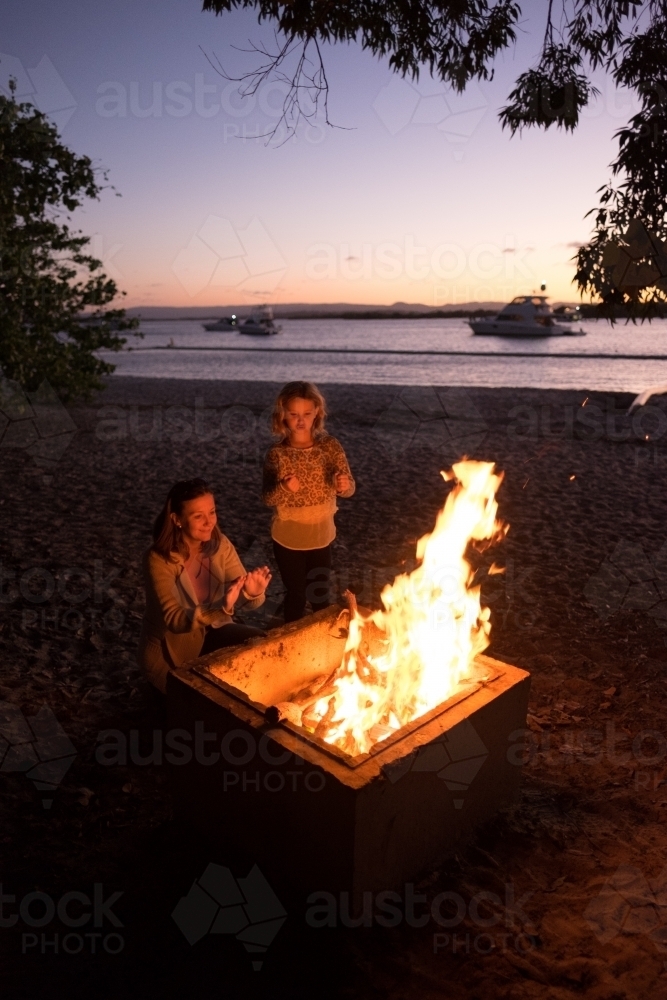 Mum and daughter sitting around camp fire - Australian Stock Image