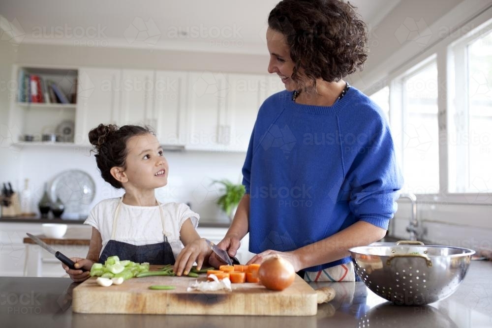 Mum and young girl chopping vegetables in kitchen - Australian Stock Image