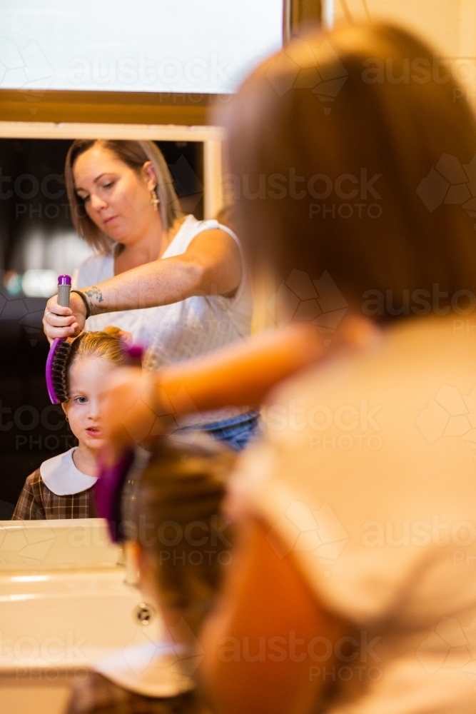 Mum brushing her daughter's hair getting child ready for school - Australian Stock Image