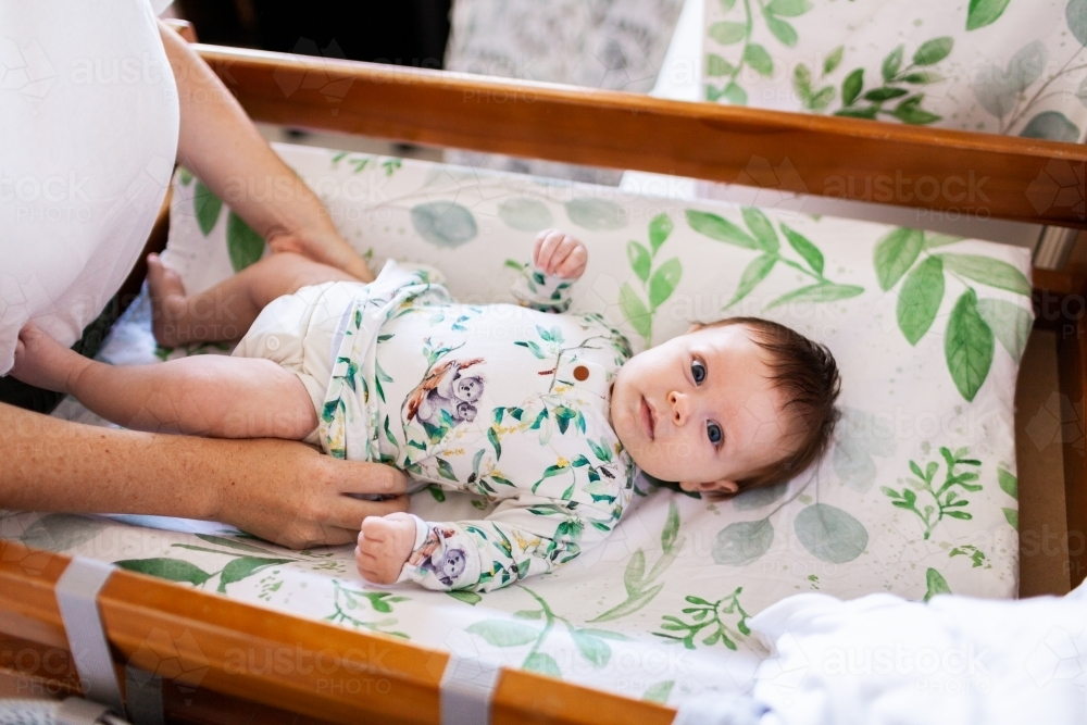 Mum getting new baby dressed on changeable smiling - Australian Stock Image