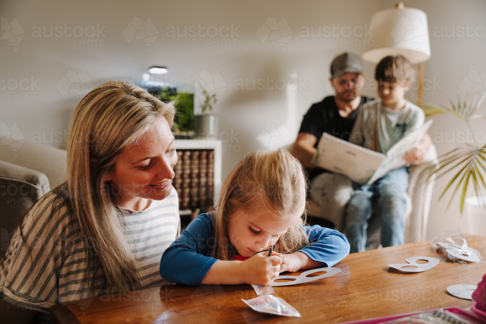 Mum helping daughter with her artwork on the table. - Australian Stock Image