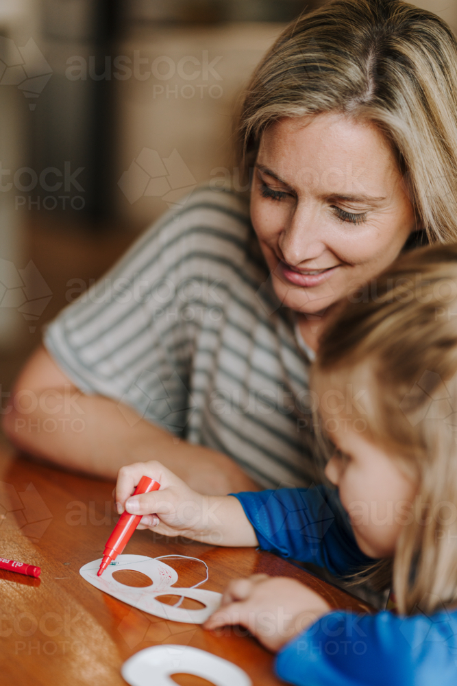 Mum helping daughter with her artwork on the table. - Australian Stock Image