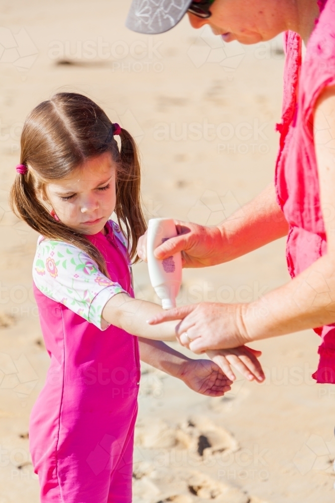 Mum helping little girl put on sunscreen to play in the sun at the beach - Australian Stock Image