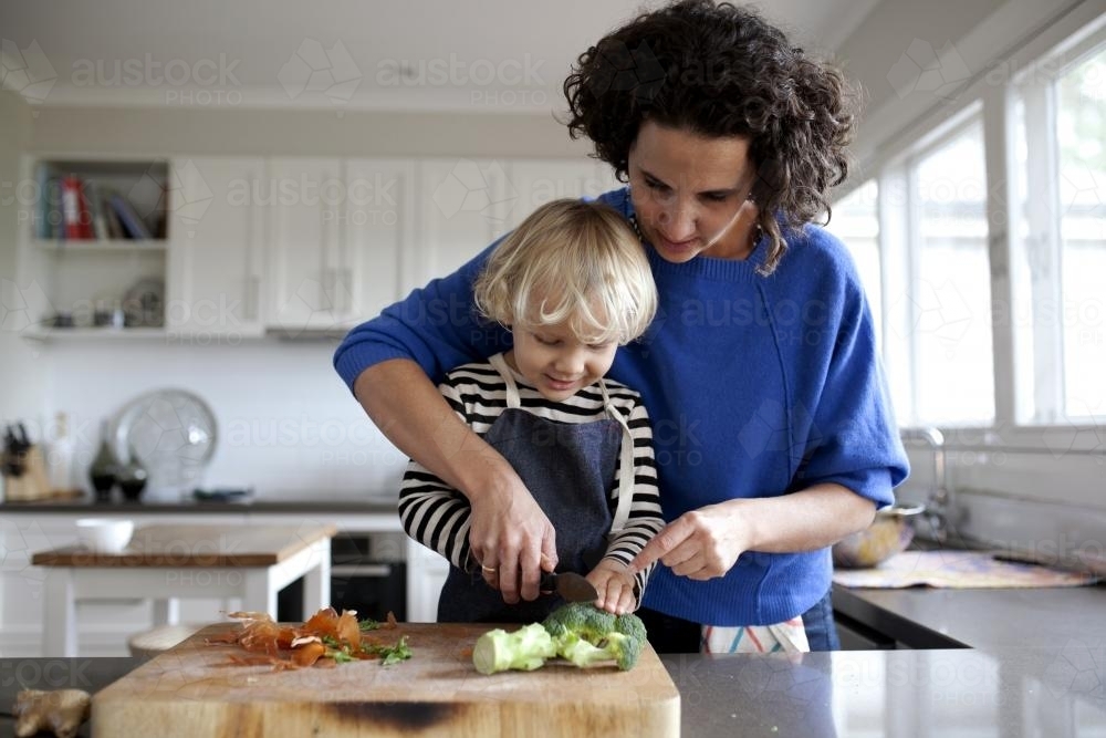 Mum helping young boy cut vegetables - Australian Stock Image