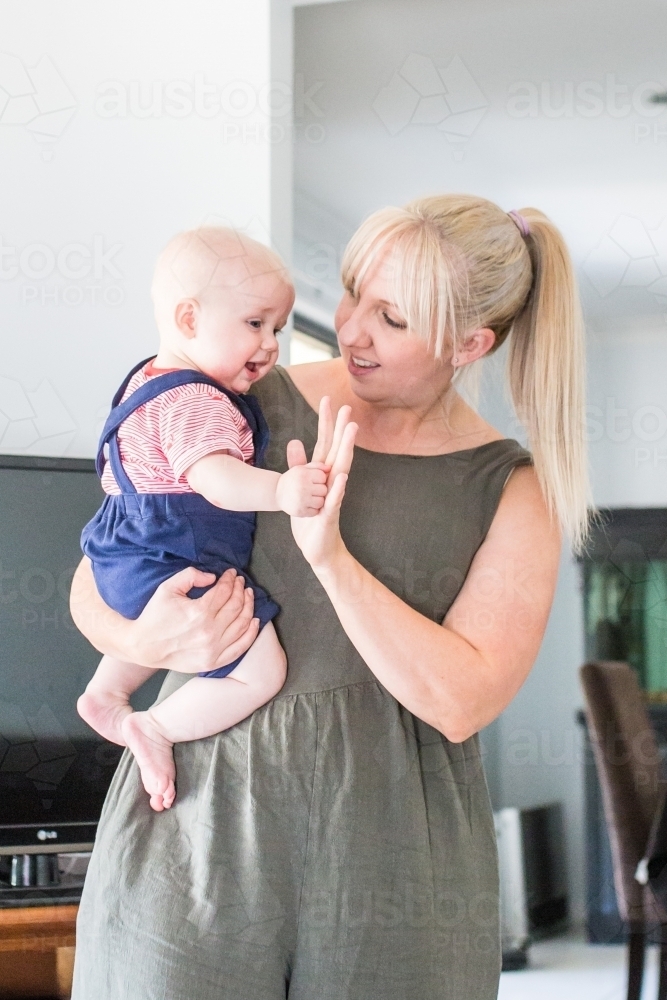 Mum holding baby boy in arms giving high five smiling - Australian Stock Image