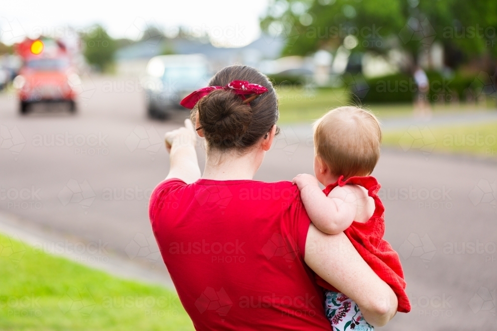 Mum holding baby to see the lolly run fire truck with Santa at Christmas time - Australian Stock Image