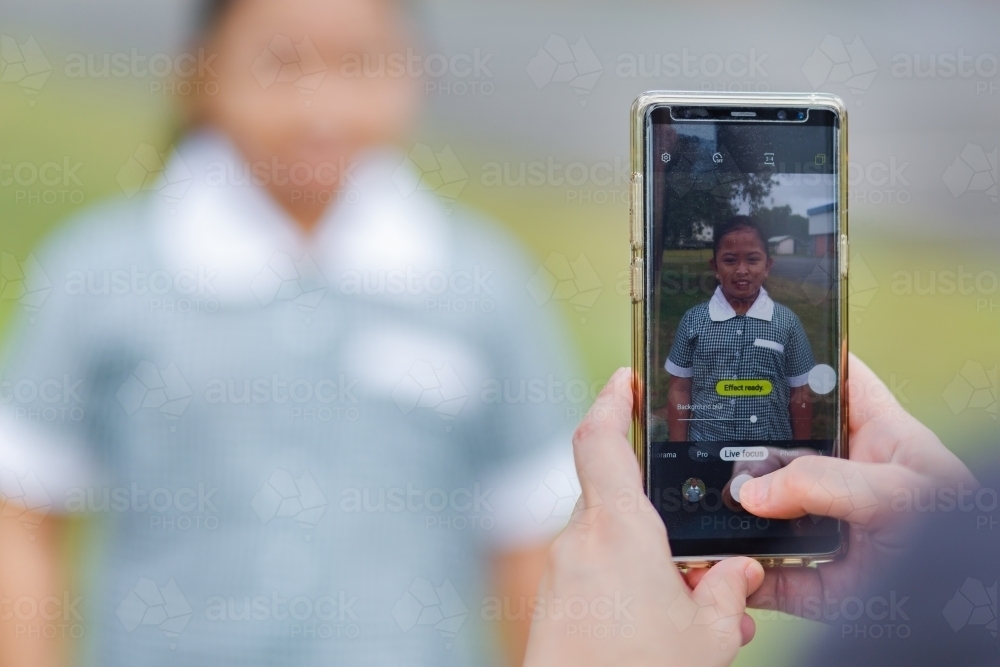 Mum holding mobile phone to take photos of her daughter on first day back to school - Australian Stock Image