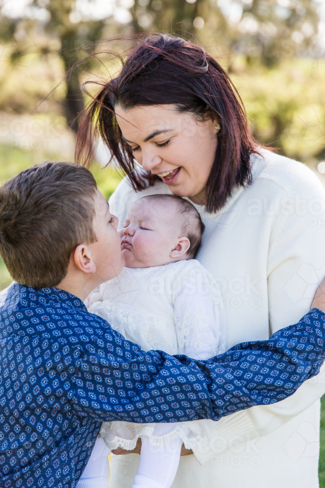 Mum holding newborn daughter while older brother kisses sister - Australian Stock Image