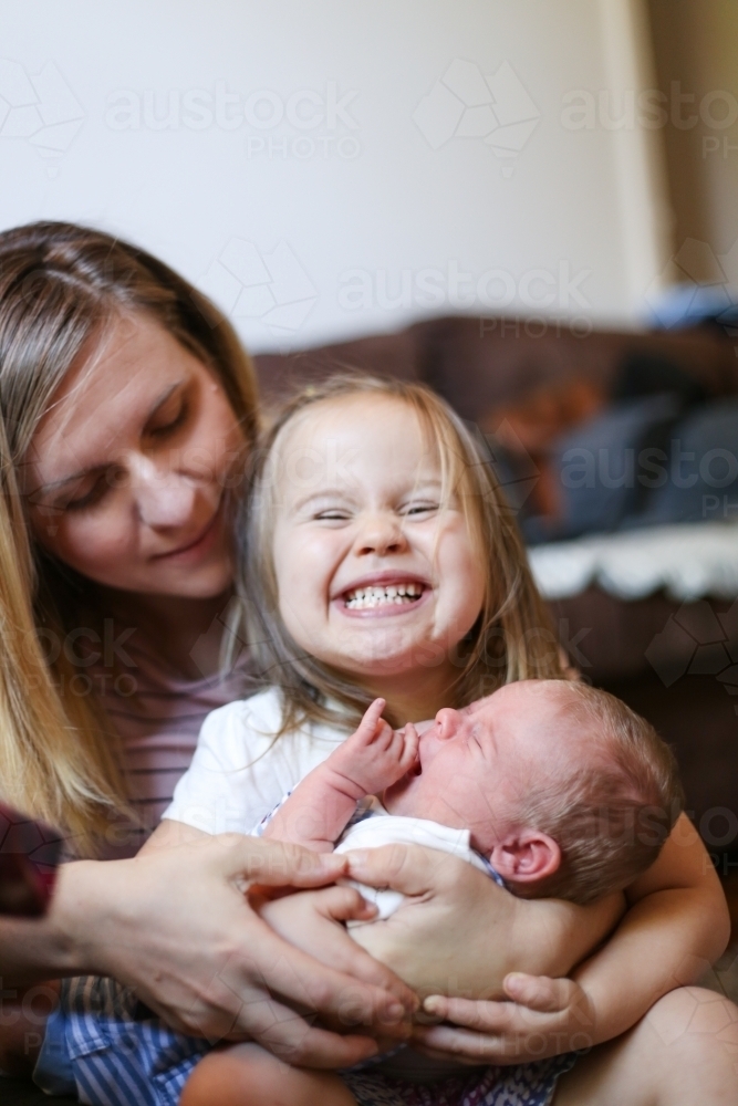Mum holds her excited daughter and newborn son on her lap - Australian Stock Image