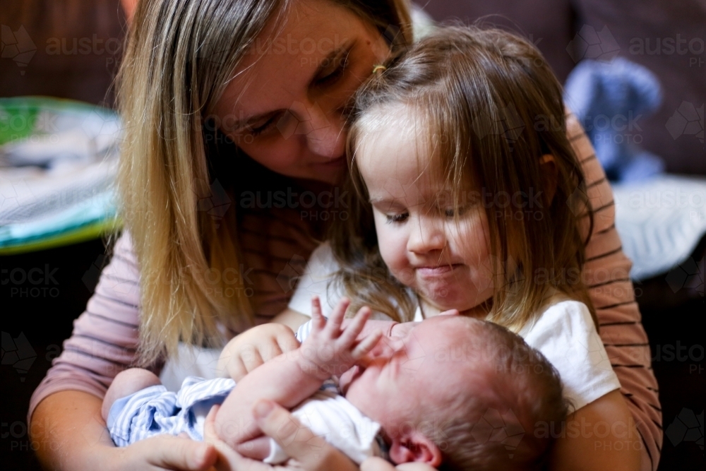 Mum holds her toddler daughter and newborn son on her lap - Australian Stock Image