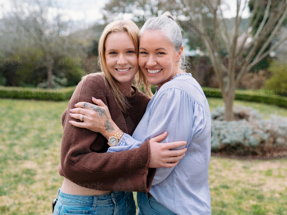 Mum hugging teenage daughter while standing in the backyard of their new home - Australian Stock Image