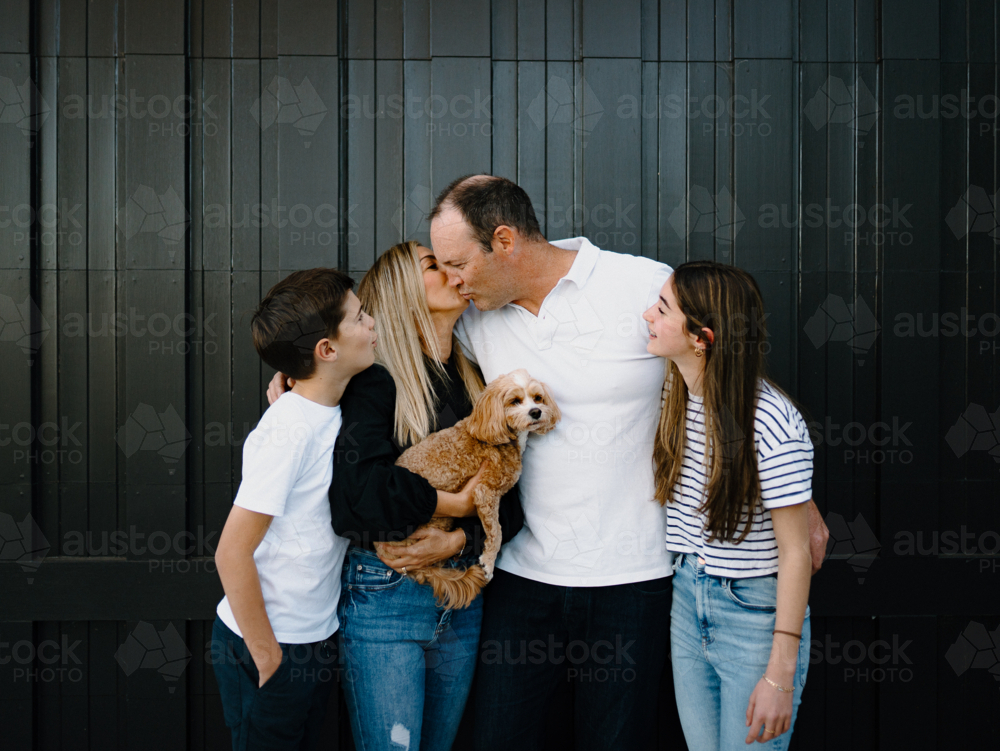 Mum kissing dad on the cheek while their kids are looking at them. - Australian Stock Image