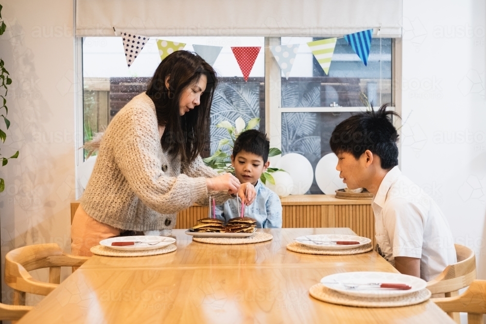 Mum lighting younger brother's birthday candles - Australian Stock Image
