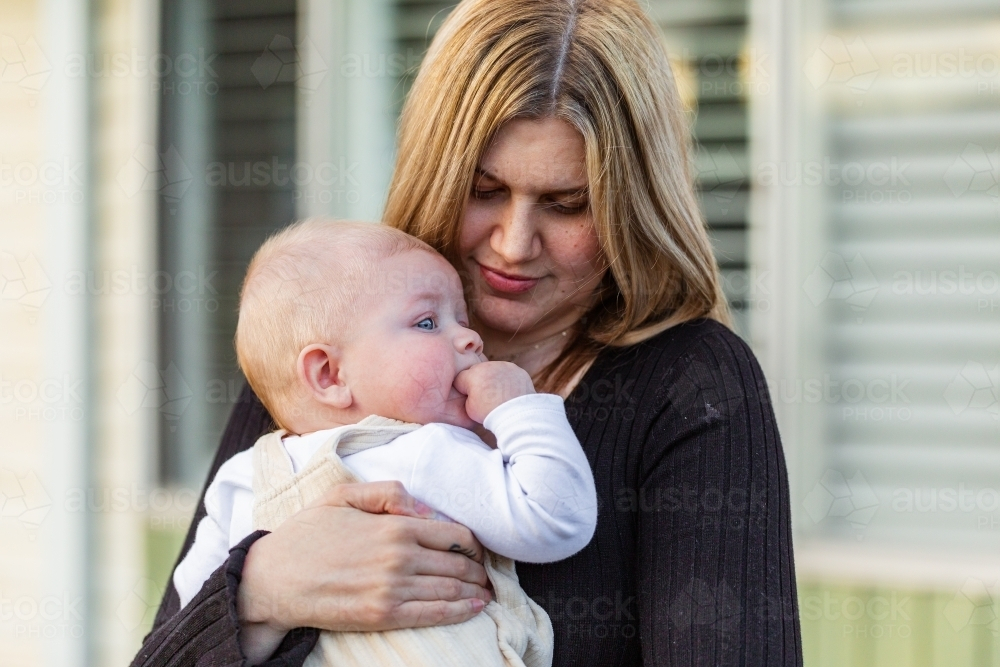mum looking down holding her young child in arms outside home - Australian Stock Image