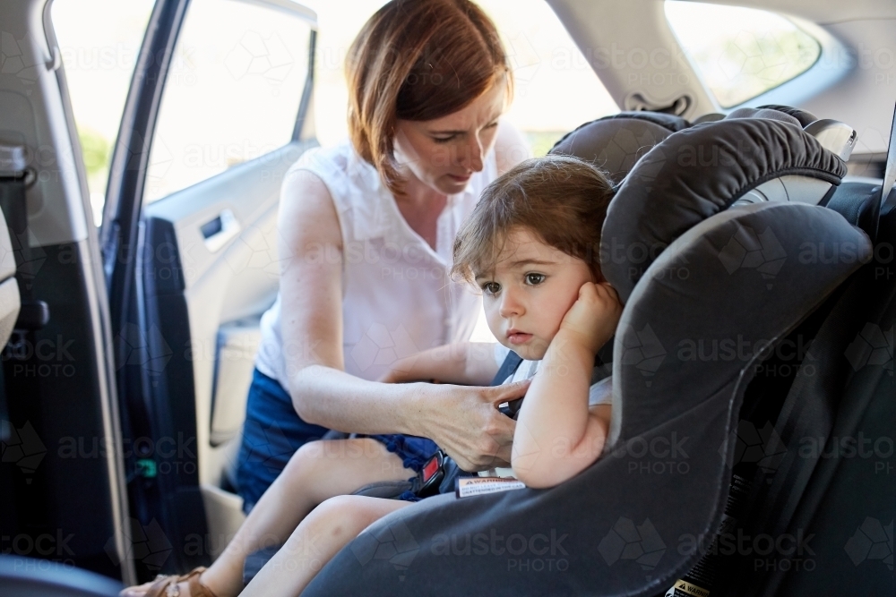 Mum putting daughter in child car seat - Australian Stock Image