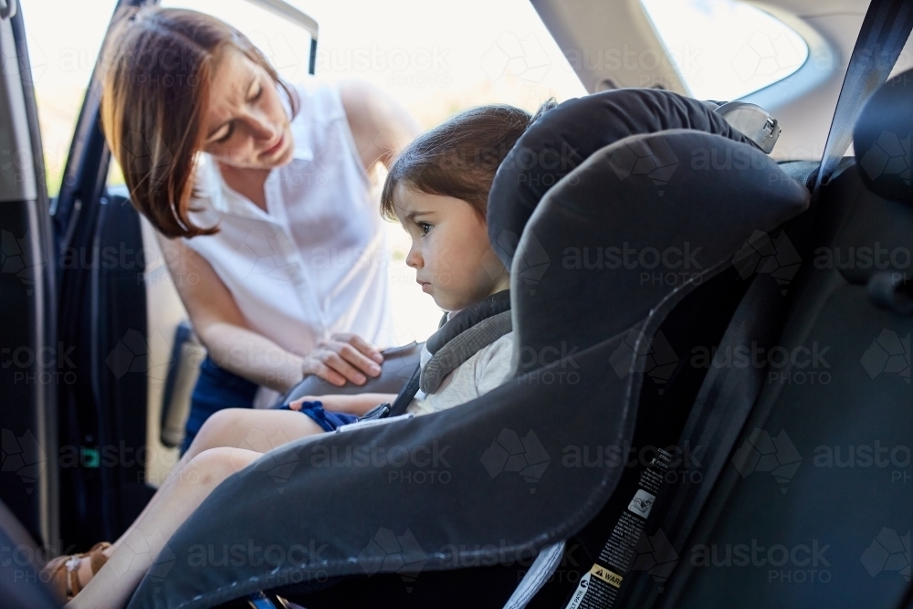 Mum putting toddler in child car seat - Australian Stock Image