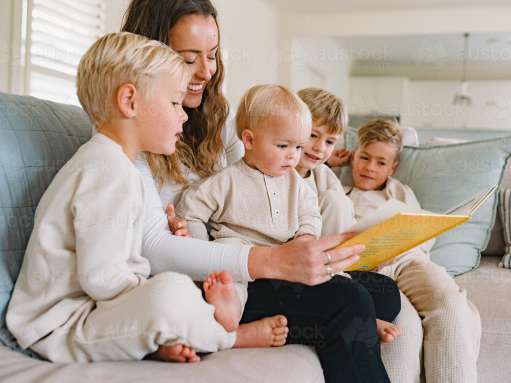 Mum reading a book to her sons seated on the couch - Australian Stock Image