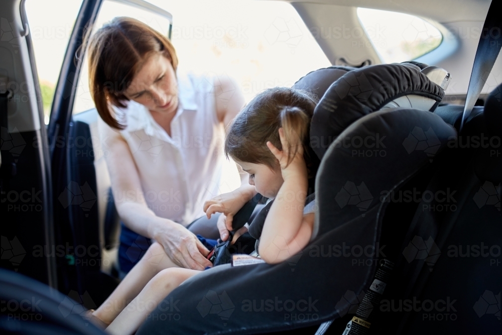 Mum strapping little girl in child car seat - Australian Stock Image