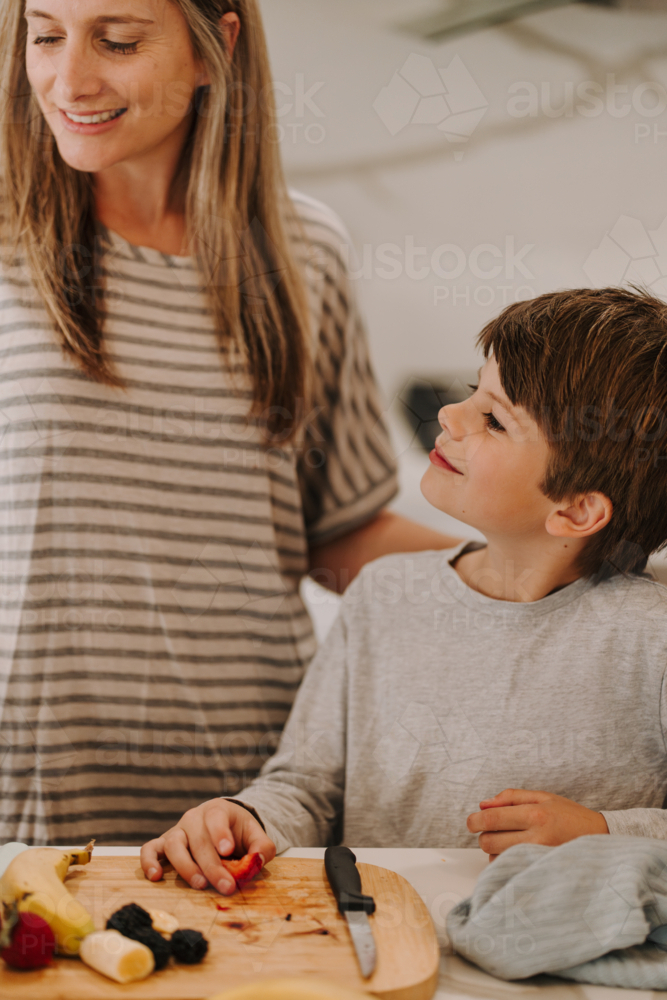 Mum teaching kid how to cut fruit in the kitchen - Australian Stock Image