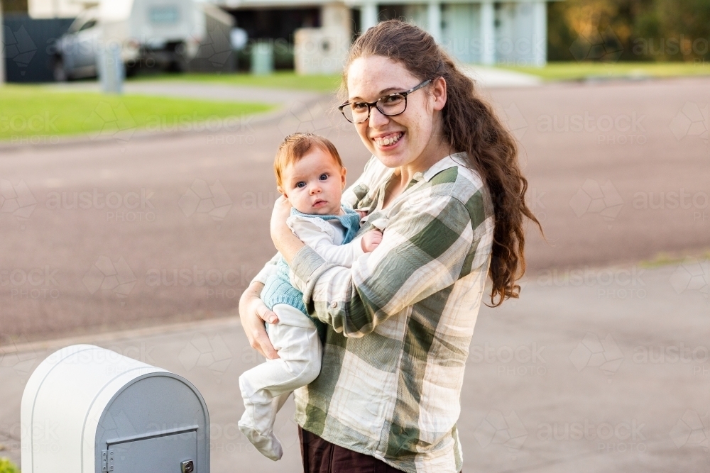 Mum with young baby checking the mailbox smiling together outside - Australian Stock Image