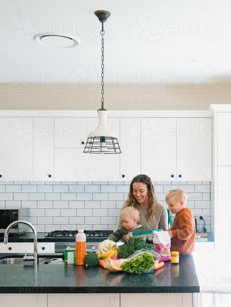 mum with young boys sitting on the kitchen counter by fresh fruits and vegetables from the shops - Australian Stock Image