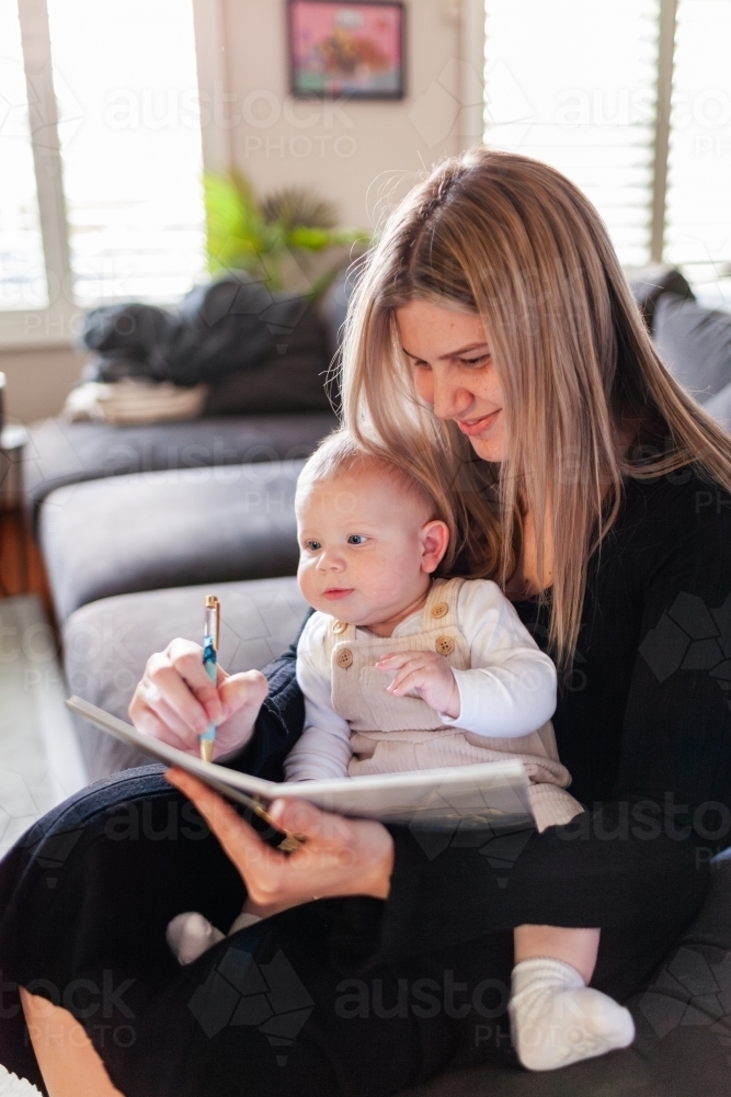 Mum working from home with baby writing in journal planner - Australian Stock Image