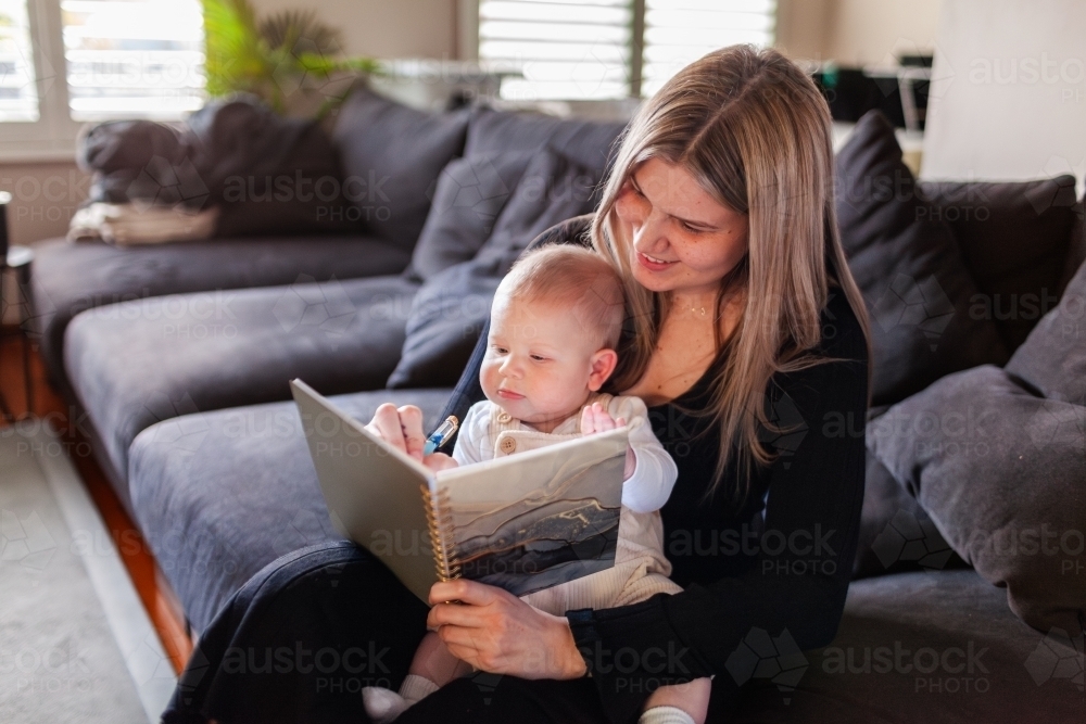 Mum working from home with baby writing in journal planner - Australian Stock Image