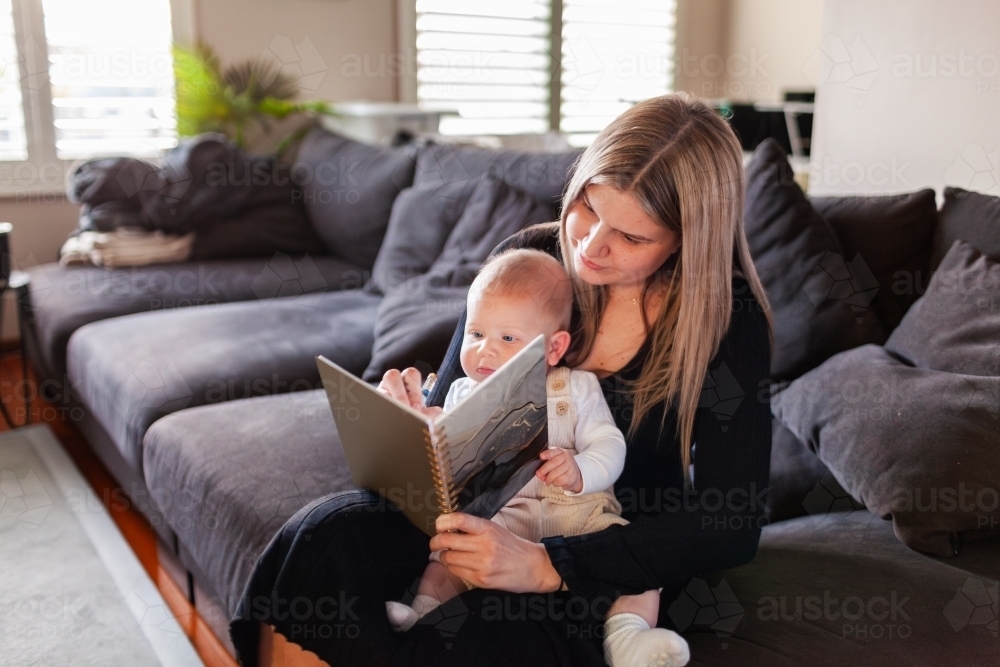 Mum working from home with baby writing in journal planner - Australian Stock Image
