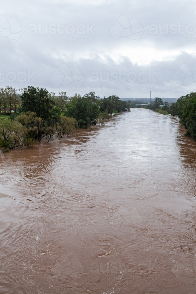 Murky swirling brown floodwaters in river during natural disaster - Australian Stock Image