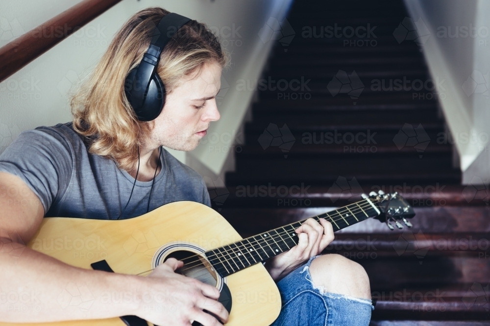 Musician playing guitar with headphones on - Australian Stock Image