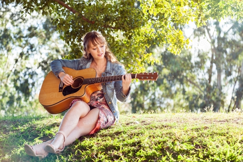 Musician sitting on a hill outside playing guitar - Australian Stock Image
