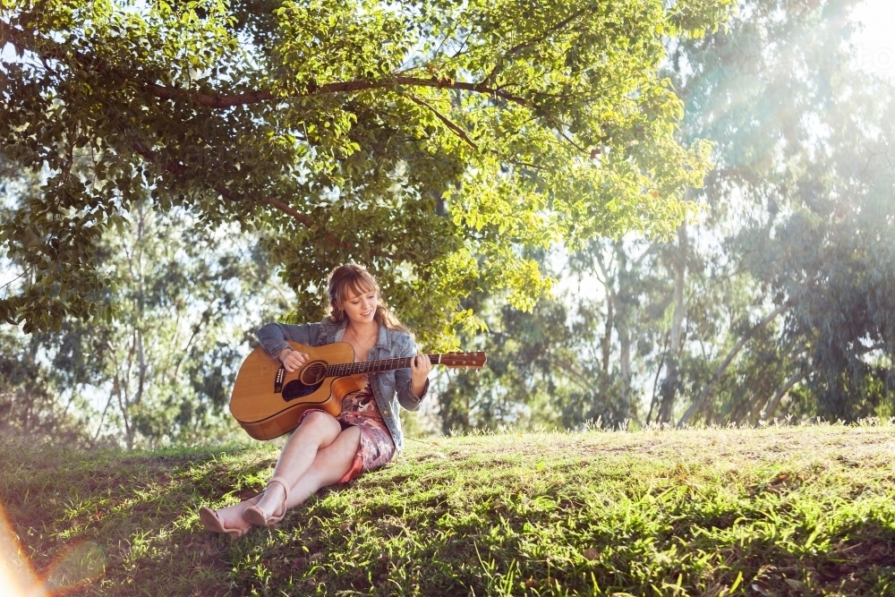Musician sitting on a hill outside playing guitar - Australian Stock Image