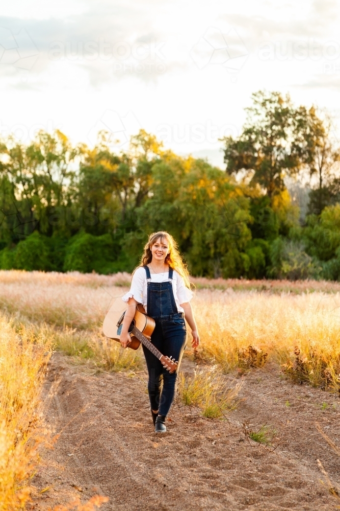 Musician with guitar walking along sandy path - Australian Stock Image