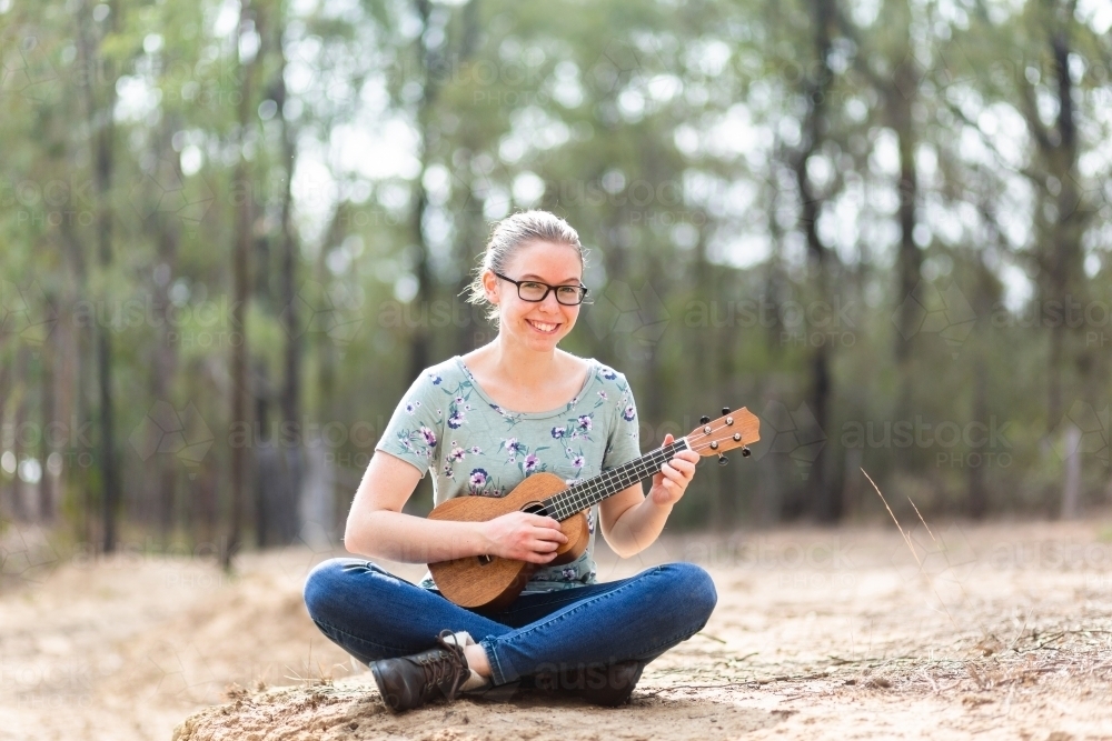 Musician with ukulele playing instrument in dry paddock - Australian Stock Image