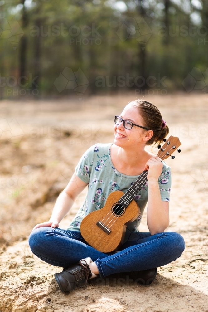 Musician with ukulele playing instrument in dry paddock - Australian Stock Image