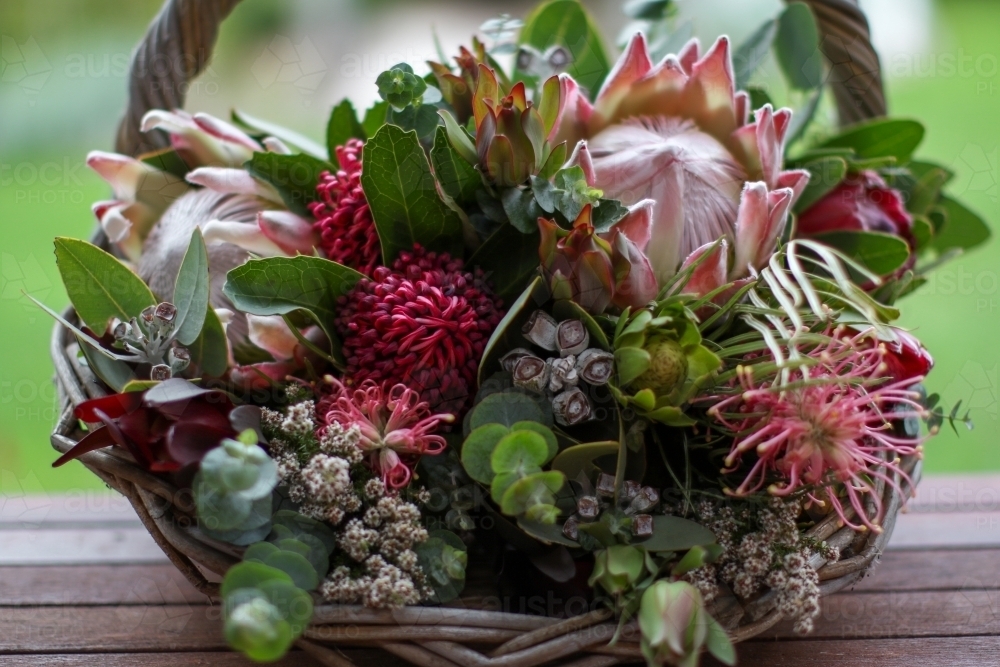 Native floral arrangement in wicker basket sitting on verandah - Australian Stock Image