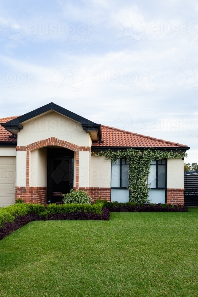 Neat and tidy front of house with flowering plant growing up between windows - Australian Stock Image