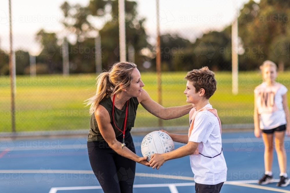 netball coach and young boy with ball training on netball court - Australian Stock Image